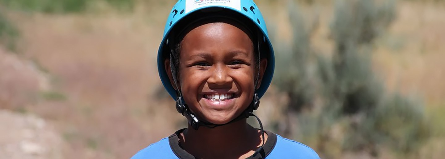 A child in helmet smiles happily at nonprofit ranch camp in Colorado