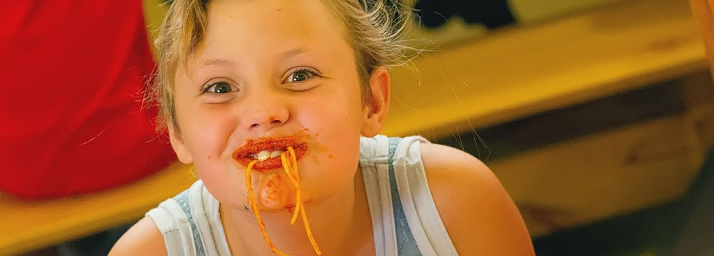 A child eats spaghetti at event fundraising for nonprofit organization