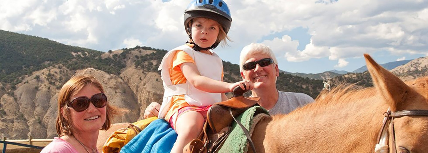 Volunteer camp counselor supervises a child riding horseback at free summer camp, Colorado