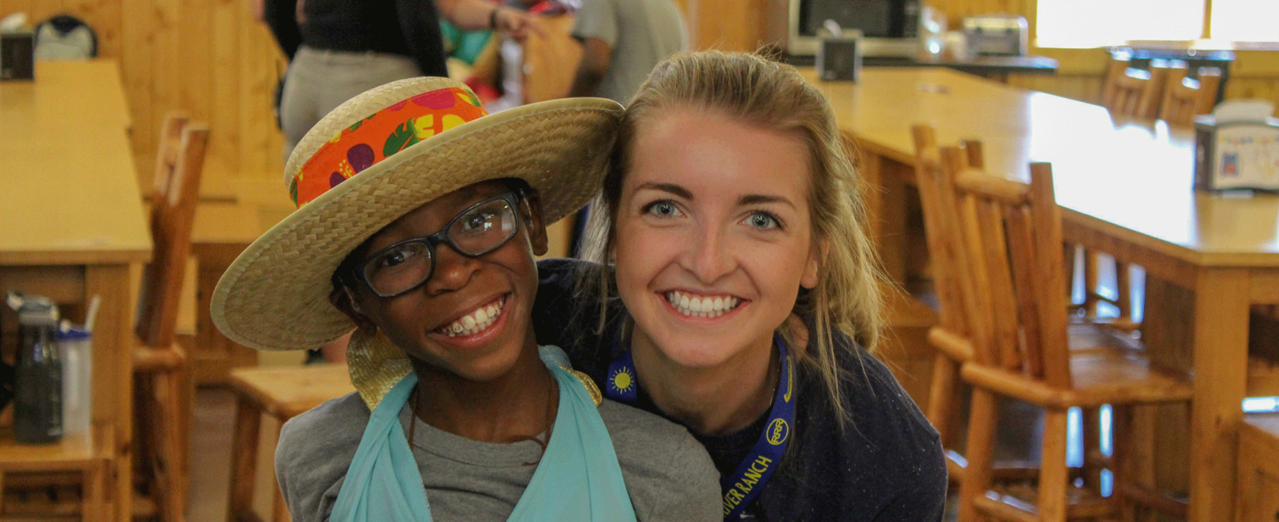 A camp volunteer and a young camper smile for a photo. Apply to be a volunteer at Roundup River Ranch.