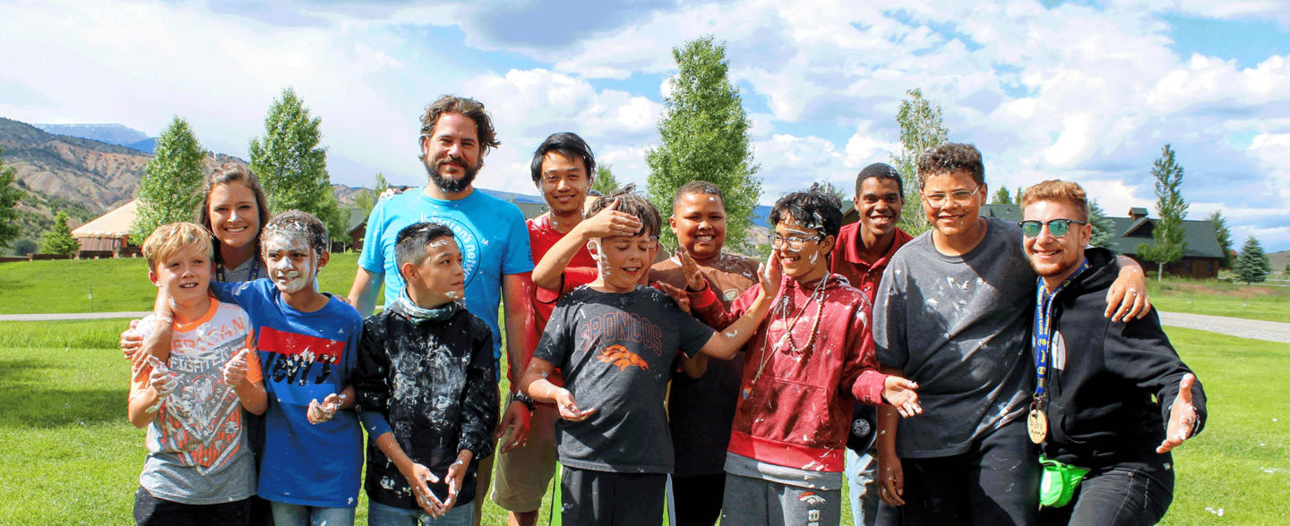 A group of campers pose for a photo with a summer camp volunteer. Support these campers at our Colorado nonprofit through summer camp donations.
